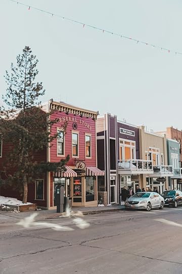 Small-town USA storefronts with a few cars parked along sidewalk.