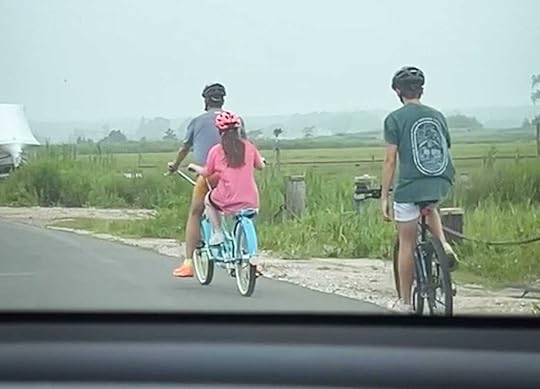 A blurry photo taken from a car of Penny pedaling on a tandem bike behind Peter. William is on another bike behind them.