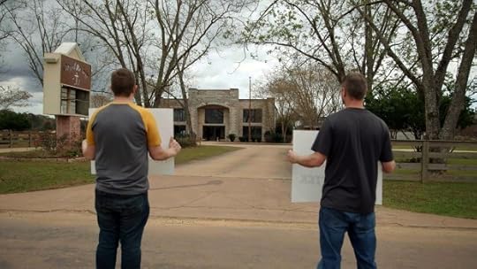 Two men face a building, holding signs.