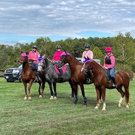 four riders wearing pink and posing with their horses