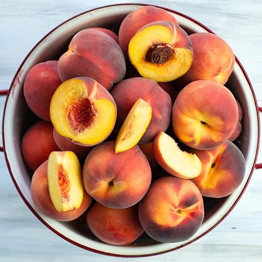 Sliced and whole fresh peaches in a metal colander.
