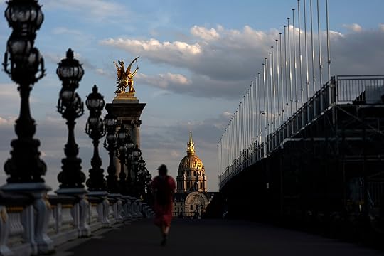 The sun sets against the Hotel des Invalides as a spectator walks on the Alexander III bridge over the Seine River, Friday, July 19, 2024, in Paris, ahead of the 2024 Summer Olympics. (AP Photo/David Goldman)