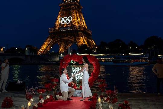 Alejandro Machuca, left, proposes to his girlfriend, Aura Guizar, both of Guadalajara, Mexico, in front of the Eiffel Tower decorated with the Olympic rings, Wednesday, July 17, 2024, while on vacation in Paris. She said yes. (AP Photo/David Goldman)
