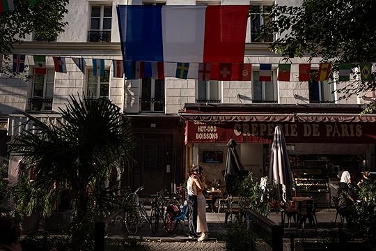 A couple embraces in the street as the flag of France hangs from a restaurant ahead of the 2024 Summer Olympics, Sunday, July 21, 2024, in Paris. (AP Photo/David Goldman)