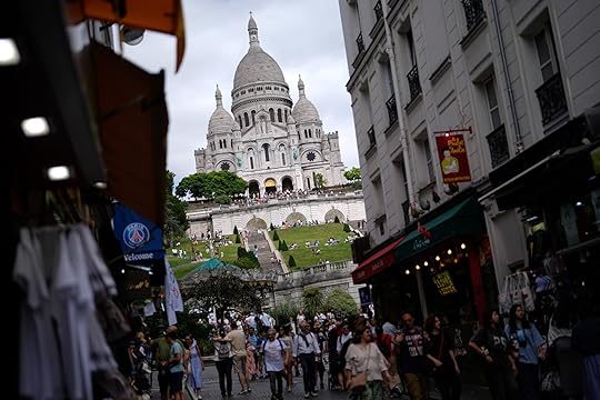 People walk past souvenir shops and restaurants below Sacre Coeur of Montmartre Basilica, ahead of the 2024 Summer Olympics, Monday, July 22, 2024, in Paris, France. (AP Photo/Rebecca Blackwell)