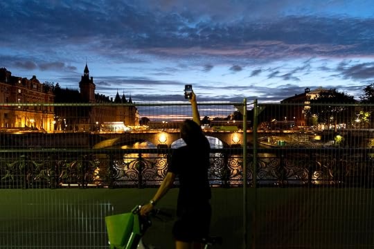 A bicyclist reaches over a security fence set up for the 2024 Summer Olympics to take a picture of the sunset as the Conciergerie building, a former prison, now used partly as a law court, stands in the background at left, Sunday, July 21, 2024, in Paris. (AP Photo/David Goldman)