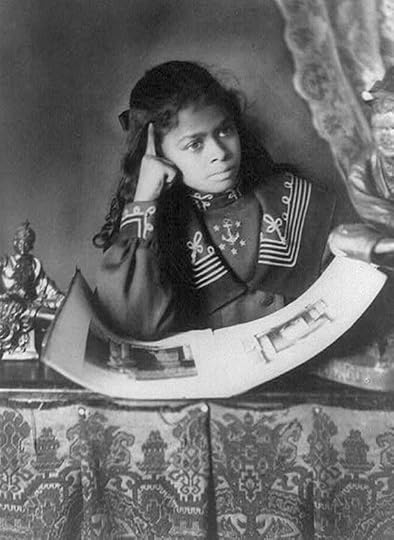 African American girl, half-length portrait, with right hand to cheek, with illustrated book on table