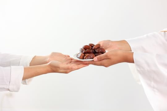 A person extending a small plate of dates to another person. Only their hands and forearms are visible and both are dressed in white.