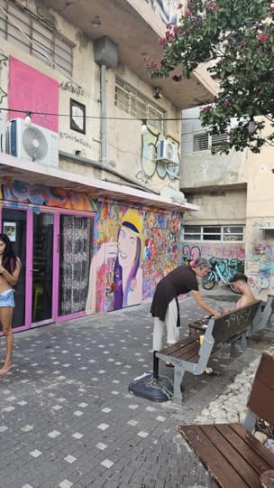 The artist bends to take more paint. In the backgtound a colorful pictures of a girl with flowing purple hair , yellow hat and flowers all aruond her. 