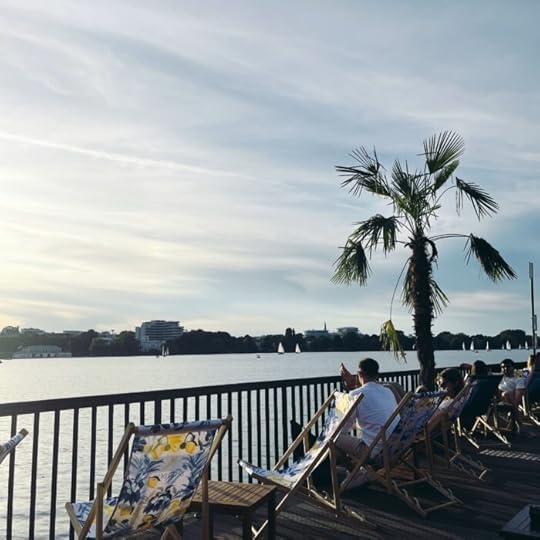 Blick von einem Steg an der Alster mit Außengastro. Liegestühle, eine Palme in einem Kübel, Abendstimmung