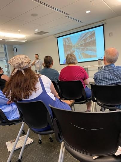 Man speaking in front of audience with a projector presentation.