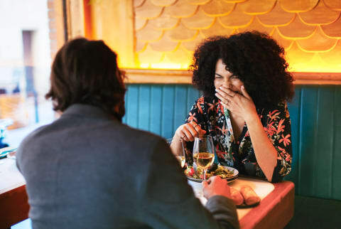 woman with hand over mouth on a date with a man at a restaurant