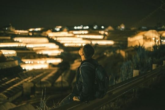 A man sitting contemplatively above lighted space at night. Why am I feeling this way?