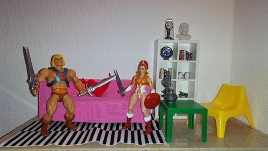 He-Man is looking at two swords in his living room, while Teela looks on.