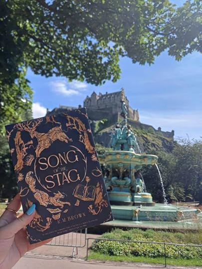 A book entitled Song of the Stag lifted up in front of a fountain with Edinburgh Castle behind it