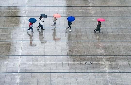 High shot looking down on a group of people with bright umbrellas walking across a stone plaza in the rain.