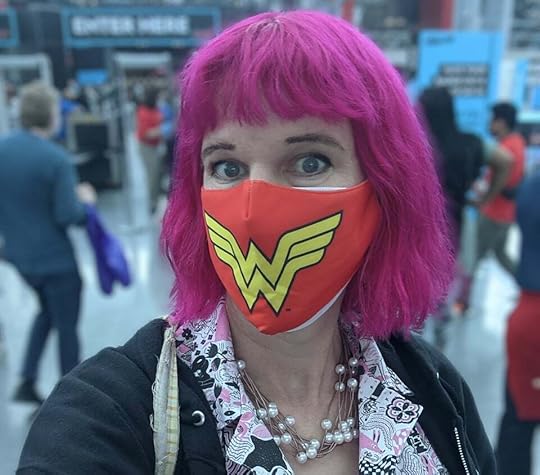 Me at a random convention a while back. I have pink hair in a bob with a fringe, and I'm wearing a Wonder Woman mask over a regular N-95. I also have a necklace with fake pearls, a cute Nooworks pink and white dress, and a black hoodie. The background is blurred.