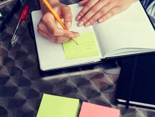 A person writing notes on a Post-it note placed in a journal, capturing creative ideas.