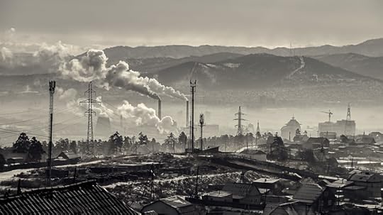 Black and white photo of factory chimneys spewing smog over a city, with mountains in the background