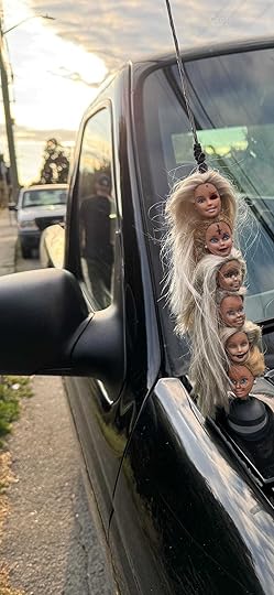 Six severed Barbie heads stuck on the antennae of a black truck.