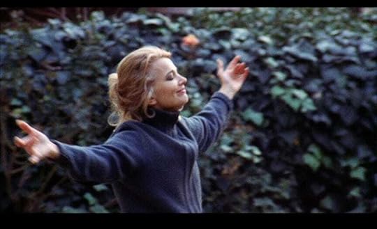 Gena Rowlands stands with her arms outstretched in front of a hedge, her eyes closed, in