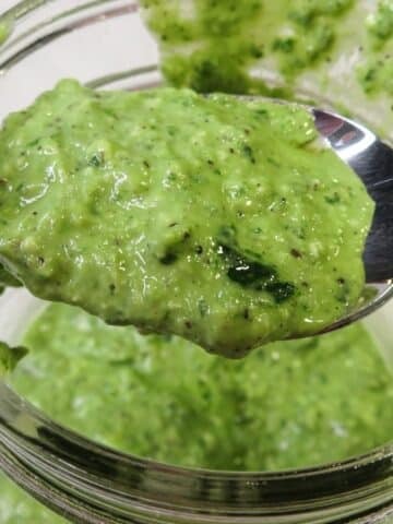Basil pesto with lemon on a spoon being scooped up from a bowl.