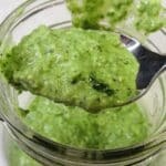 Basil pesto with lemon on a spoon being scooped up from a bowl.