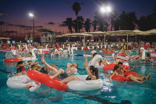 A lively evening pool party with many people enjoying themselves on inflatable swan floats in a large swimming pool. The scene is set against a beautiful sunset, with palm trees silhouetted in the background and lights illuminating the area. Some people are splashing water and laughing, creating a fun and festive atmosphere.