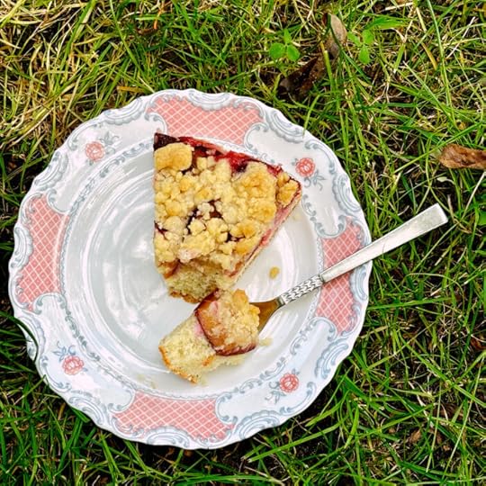 Ein angeschnittenes Stück Pflaumenkuchen auf einem sehr altmodischen Kuchenteller, der im Gras steht
