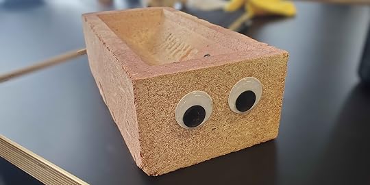 A photo of a brick sitting on an office desk. The brick has two googly eyes stuck to the front.