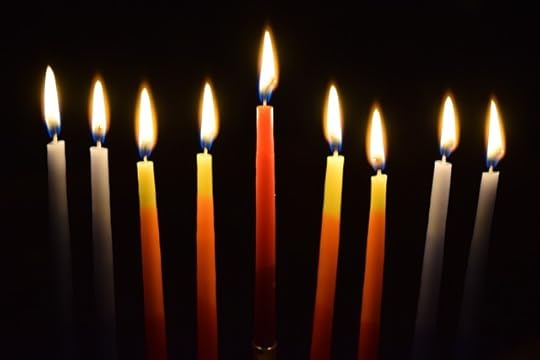 A row of 9 illuminated candles. Center cande is red. Next two in either direction are yellow and orange. Outer candles are white.