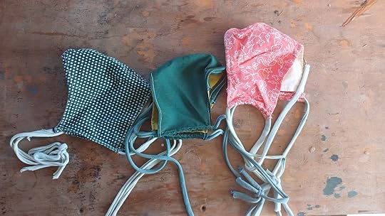 hree home made cloth masks with cloth ties. One pink with a white floral pattern, one dark green with yellow lining, and one green with white dots.