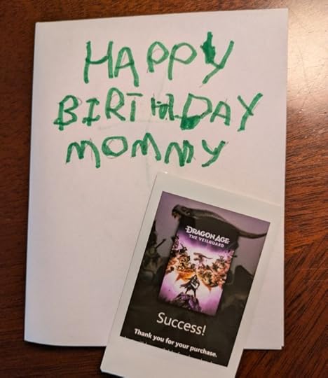a kid drawn birthday card that says "Happy Birthday Mommy" with a small Polaroid and a picture of a Dragon Age Veilguard pre-order