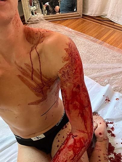 David sitting on their floor in black underwear with blood on their left arm, chest, and neck
