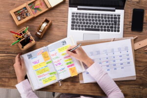 Image of a desk including calendar, laptop and schedule with sticky tabs