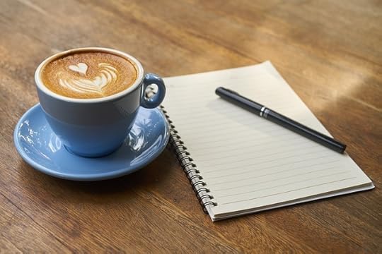 Blue coffee cup with cofee beside an open notebook and pen on a wooden table.