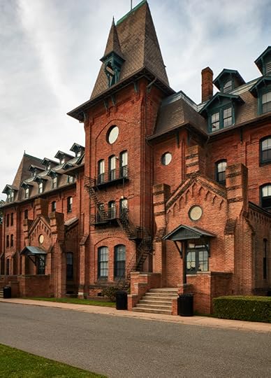 Medium shot of the entrance to a long, three-story red brick building with sharply steeped roofs.