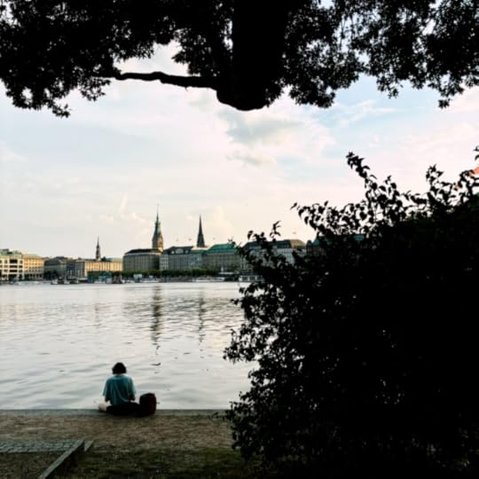 Blick über die Binnenalster in Richtung Rathaus. Eine Frau sitzt im Vordergrund am Ufer, mit dem Rücken zum Betrachter. Sommerabendstímmung.