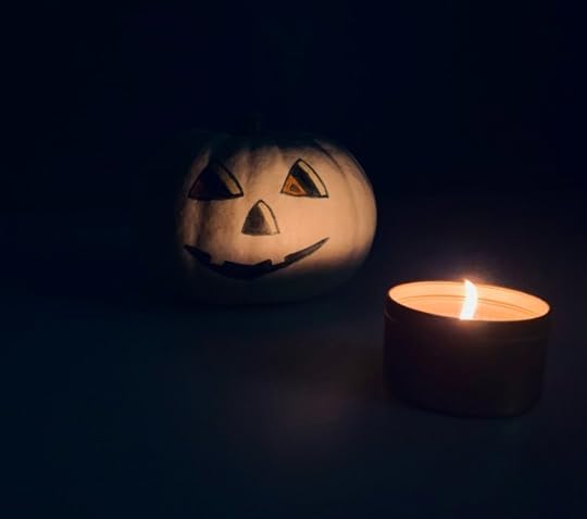 My white pumpkin with a painted jack-o’-lantern face in shadow, partly lit by a candle in the dark.