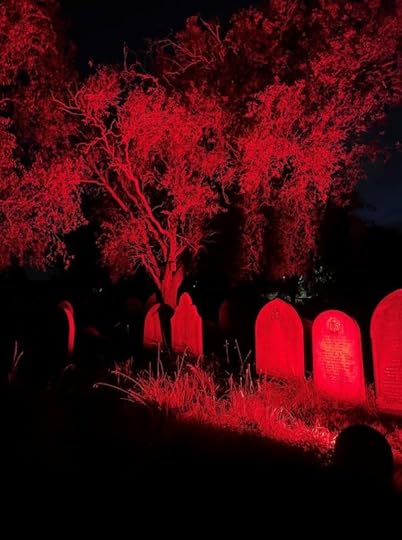 Image shows a row of gravestones and trees lit up red