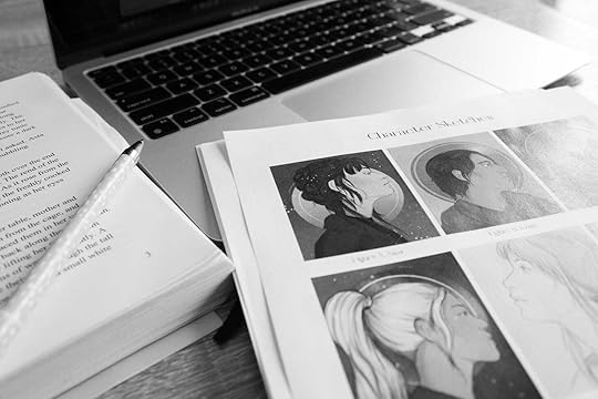 Black and white image of a laptop, a bound manuscript and a page of character illustrations.