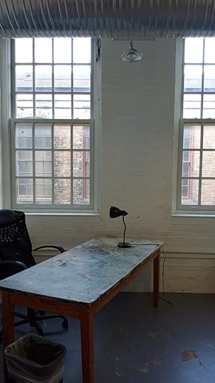 Empty studio space with large windows, table, lamp, and chair