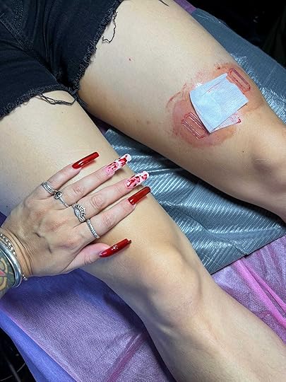 Jade's hand (with acrylics designed to look like blood spatters) rests on my right thigh, while my left has a fresh cutting that spells my name.