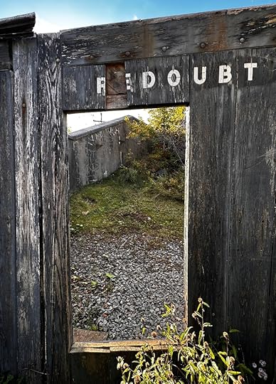 A door in the wooden wall, with white lettering above saying “REDOUBT”