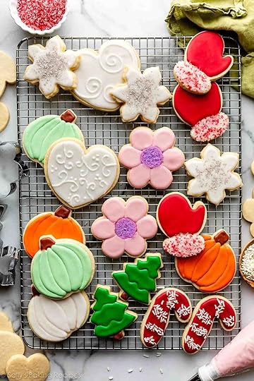 Decorated sugar cookies including pink flowers, white hearts, red mittens, orange pumpkins, and green trees on wire cooling rack.