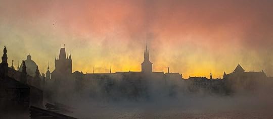 A misty Charles Bridge silhouetted by a pink and orange sunrise. 