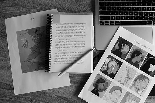 Black and white flat lay of a bound manuscript, illustrations on A4 paper and a laptop.