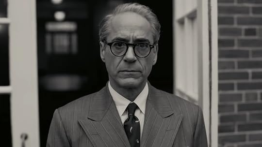 Robert Downey Jr. in glasses and a suit standing near a doorway in a black and white scene from Oppenheimer