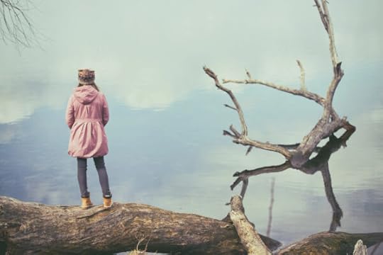 teen in a pink jacket stands by a dead tree looking out across a misty valley