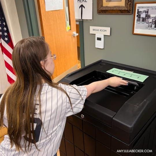 Penny is placing an her ballot into a black ballot drop box.